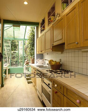 Picture - Oven and dishwasher in fitted galley kitchen with wooden flooring and small conservatory extension. Fotosearch