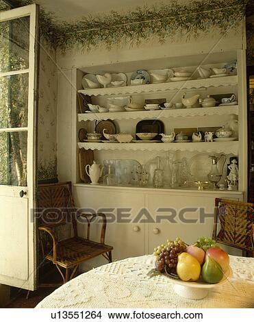 Painted flowers above alcove with white crockery on shelves in dining room with ceramic fruit in bowl on lace tablecloth View Large Photo Image Picture - Painted flowers above alcove with white crockery on shelves in dining room with ceramic fruit in bowl on lace tablecloth. Fotosearch