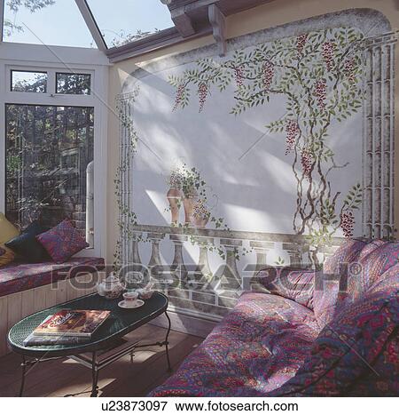 Painted mural on wall of conservatory living room with patterned sofa and metal table View Large Photo Image Stock Photo - Painted mural on wall of conservatory living room with patterned sofa and metal table. Fotosearch