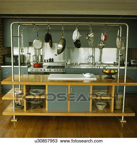 Stock Image - Pans suspended from steel frame on large wooden island unit in modern kitchen. Fotosearch