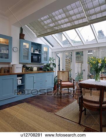 Stock Image - Pastel blue fitted cupboards in kitchen extension with sisal mats on wooden flooring and blinds on glass ceiling. Fotosearch