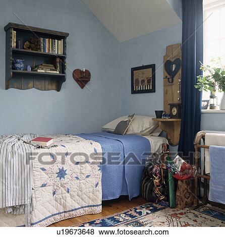 Patchwork quilt and blue sheet on bed in pastel blue Shaker-inspired bedroom with small wooden shelves above the bed View Large Photo Image Stock Photo - Patchwork quilt and blue sheet on bed in pastel blue Shaker-inspired bedroom with small wooden shelves above the bed. Fotosearch