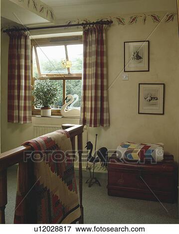 Stock Photo - Patchwork quilts on bannisters and wooden chest on small landing with checked curtains at the window. Fotosearch
