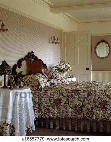 Stock Photo - Patterned quilt and matching cushions on antique Victorian mahogany bed in country bedroom with beige wallpaper. Fotosearch
