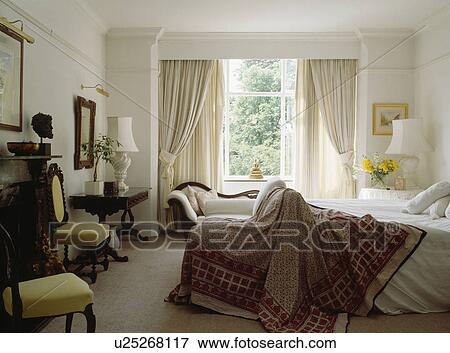 Stock Photo - Patterned throw on bed in white bedroom with cream curtains. Fotosearch