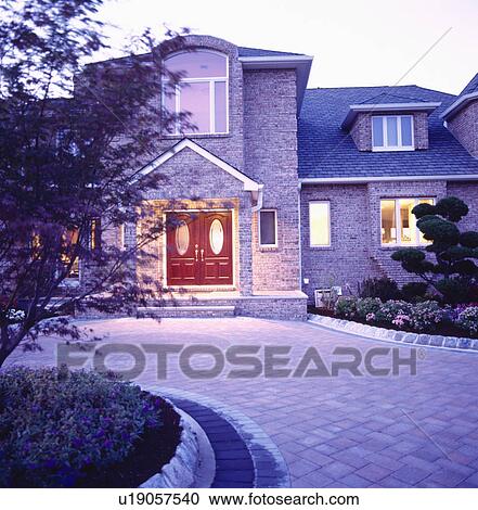 Stock Image - Paved drive to newbuild house with lighted windows in early evening. Fotosearch