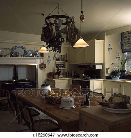 Pendant lighting and utensil rack above rectangular wooden table in neutral country kitchen View Large Photo Image Stock Photo - Pendant lighting and utensil rack above rectangular wooden table in neutral country kitchen. Fotosearch