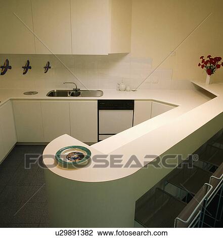 Stock Image - Peninsular unit in modern white kitchen with flush cupboard doors. Fotosearch