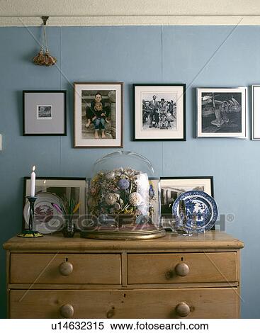 Stock Photography - Photographs on wall above pine chest of drawers with Victorian glass dome . Fotosearch
