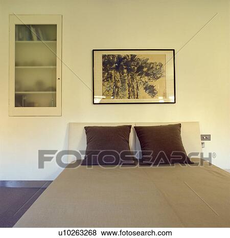 Stock Photo - Picture above bed with brown velvet cushions in modern bedroom with frosted glass door on flush-fitted bookcase. Fotosearch