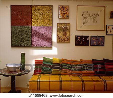 Stock Photo - Pictures above sofa with colourful cushions and yellow checked blanket. Fotosearch