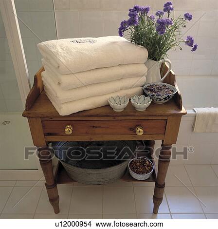Picture - Pile of white towels and blue cornflowers in jug on small antique pine table with drawers. Fotosearch