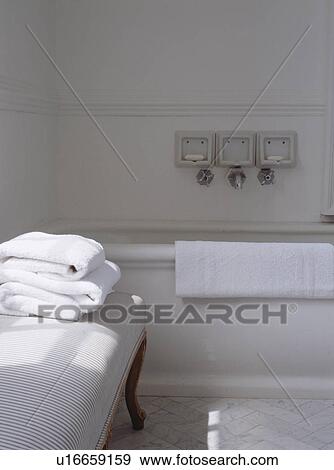 Stock Photo - Pile of white towels on upholstered striped stool in traditional white bathroom. Fotosearch