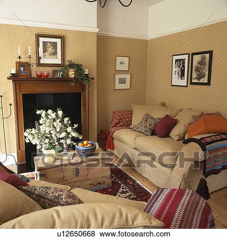 Stock Photo - Pine chest in front of fireplace in livingroom withcream sofas and white cornice above patterned beige wallpaper. Fotosearch