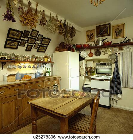 Stock Photograph - Pine table and chair in old-fashioned kitchen with freestanding fridge-freezer and electric oven. Fotosearch