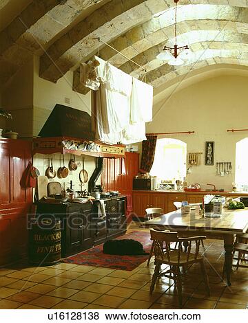 Pine table and chairs in basement kitchen with large black Aga and arched ceiling View Large Photo Image Stock Photo - Pine table and chairs in basement kitchen with large black Aga and arched ceiling. Fotosearch