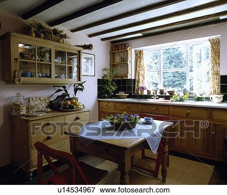 Stock Photo - Pine table and chairs in cottage kitchen with pine chest of drawers and wooden fitted cupboards. Fotosearch