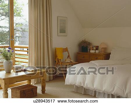 Pine table and cream duvet on bed in neutral bedroom with glass doors to balcony View Large Photo Image Stock Photo - Pine table and cream duvet on bed in neutral bedroom with glass doors to balcony. Fotosearch