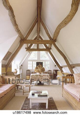 Stock Photo - Pine wood sofas with pink cushions in openplan attic living and dining room with large beams on apex ceiling. Fotosearch