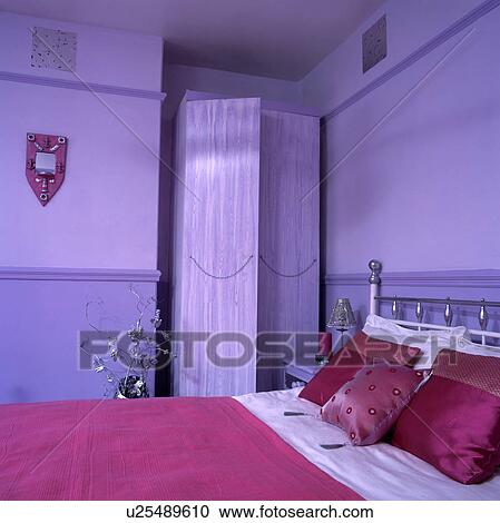Stock Image - Pink silk cushions and pink bedcover on bed in mauve bedroom with mauve painted wardrobe . Fotosearch