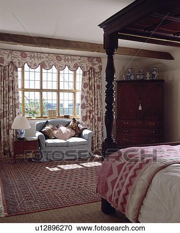 Pink+white quilt on four-poster bed in country bedroom with blue sofa in front of window with pink+white curtains View Large Photo Image Stock Image - Pink+white quilt on four-poster bed in country bedroom with blue sofa in front of window with pink+white curtains. Fotosearch