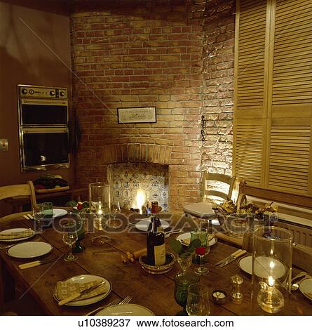 Place settings and lighted candles on wooden table in kitchen with fireplace in brick wall View Large Photo Image Stock Photo - Place settings and lighted candles on wooden table in kitchen with fireplace in brick wall. Fotosearch