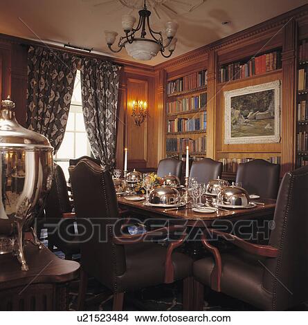 Picture - Place settings and silver dishes on table in traditional hotel restaurant with leather chairs. Fotosearch