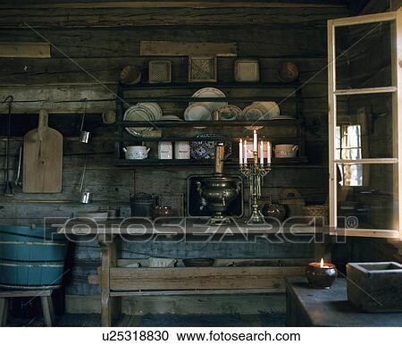 Stock Image - Plates on wooden shelves above wooden table in rustic wooden kitchen. Fotosearch