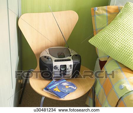 Picture - Portable stereo and CDs on a chair beside a bed in a contemporary orange and green bedroom. Fotosearch