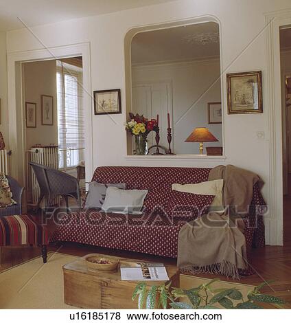 Stock Photo - put-you-up sofa with red and white spotted throw and cushions in painted white room with wooden chest and parket floor. . Fotosearch