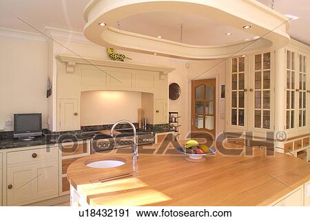Stock Image - Recessed halogen lights in suspended frame above island unit with small sink underset in wood worktop. Fotosearch
