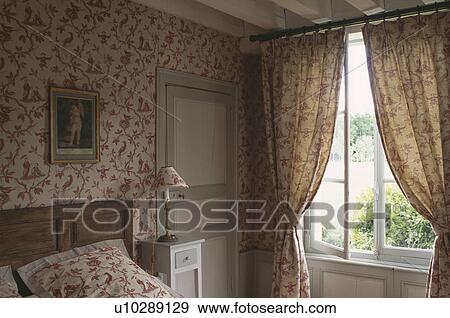 Red Patterned Wallpaper And Matching Curtains In Country Bedroom Stock Photo