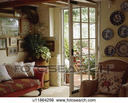 Stock Photo - Red sofa beside glazed door to conservatory in cottage living room. Fotosearch
