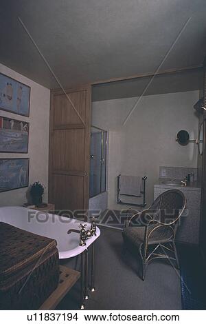 Rolltop bath with brass taps in bathroom with cane chair View Large Photo Image Picture - Rolltop bath with brass taps in bathroom with cane chair. Fotosearch