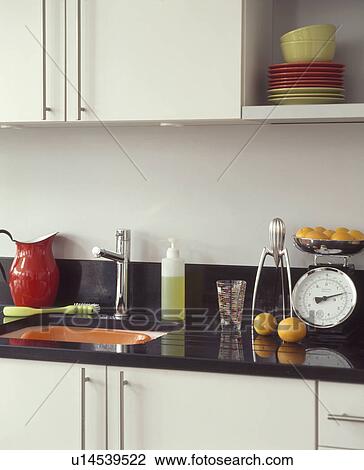 Stock Image - Scales and chrome Alessi juicer on black granite worktop in modern white kitchen. Fotosearch