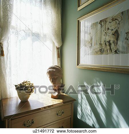 Sculpture head on pine chest-of-drawers below white voile curtains in corner of a pastel turquoise room View Large Photo Image Stock Image - Sculpture head on pine chest-of-drawers below white voile curtains in corner of a pastel turquoise room. Fotosearch