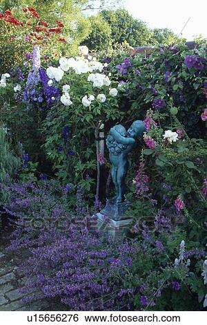 Stock Photograph - Sculpture in scented flowering borders in country garden in summer. Fotosearch