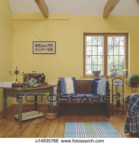 Sewing machine on table beside wooden settle with blue cushions below window in yellow living and workroom View Large Photo Image Stock Photograph - Sewing machine on table beside wooden settle with blue cushions below window in yellow living and workroom. Fotosearch