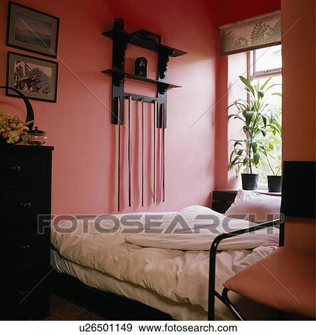 Small black shelves on wall in pink bedroom with green houseplants on windowsill above bed View Large Photo Image Stock Photo - Small black shelves on wall in pink bedroom with green houseplants on windowsill above bed. Fotosearch