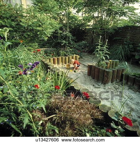 Stock Photograph - Small boy playing in sandpit in town garden in summer. Fotosearch