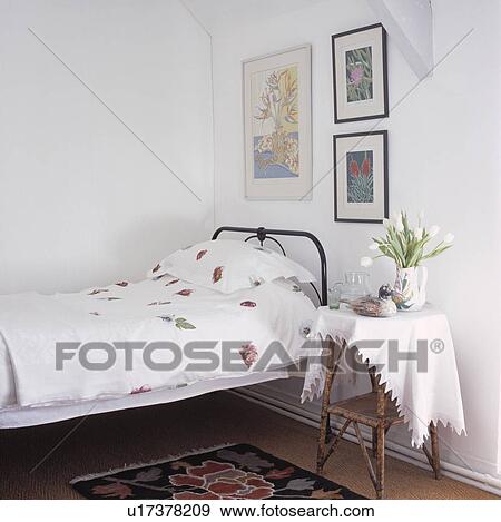 Small traditional white bedroom with black bed frame and cane side table View Large Photo Image Stock Photo - Small traditional white bedroom with black bed frame and cane side table . Fotosearch