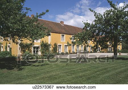 Stock Photo - Small trees on lawn in front of ochre painted country house. Fotosearch
