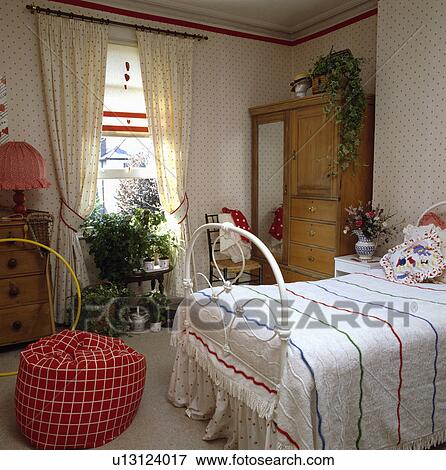 Spotted wallpaper and matching curtains at window in bedroom with red beanbag and white bed with striped cover View Large Photo Image Stock Photo - Spotted wallpaper and matching curtains at window in bedroom with red beanbag and white bed with striped cover. Fotosearch