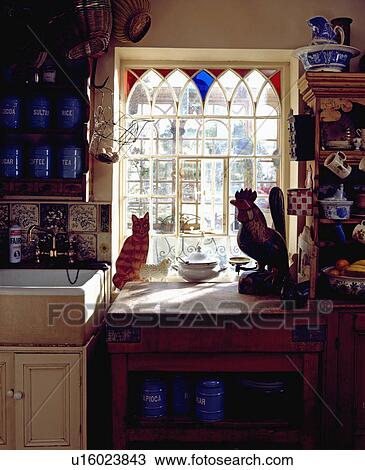 Stock Image - Stained glass border on window above old butcher's block with cat and cockerel ornaments . Fotosearch