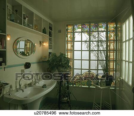 Stock Photograph - Stained glass window in dark traditional bathroom with lighted lamps above double basin. Fotosearch
