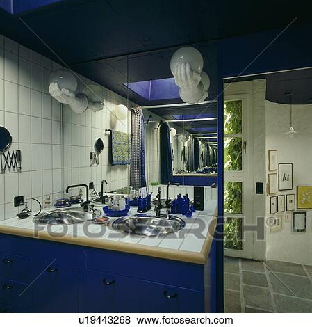 Stock Photo - Stainless steel double basins in fitted blue vanity unit in blue bathroom with white wall tiles. Fotosearch