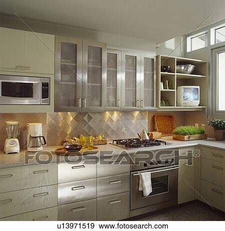 Stock Photo - Stainless steel fitted cupboards and drawers and pale grey wood cupboards in modern kitchen with corian counter. Fotosearch