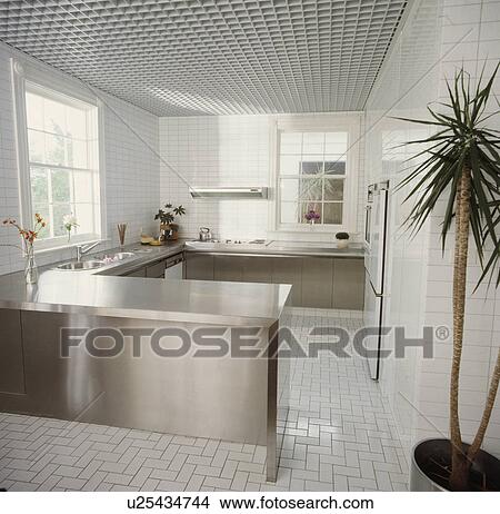 Picture - Stainless steel fitted cupboards in modern kitchen with white tiled walls and floor and white grid ceiling. Fotosearch
