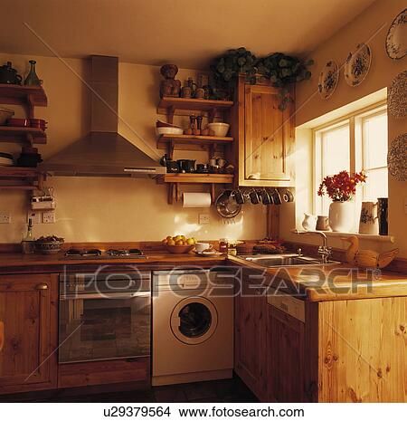 Picture - Stainless steel oven and white washing machine below extractor in small wood kitchen with fitted dishwasher. Fotosearch