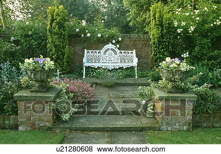 Stock Photo - Stone steps to white bench on small paved patio in country garden in summer. Fotosearch